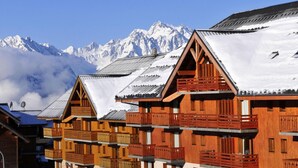 Une rangée de chalets en bois dotés de balcons, se dressant sur fond de montagnes enneigées.