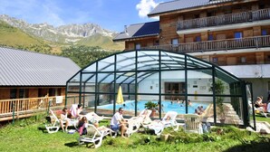 A chalet with a glass-enclosed pool area, surrounded by lush greenery and mountains in the background. - 200m from ski slopes, swimming pool, sauna, balcony, tv, ski locker, 25-27m² (Saint-François-Longchamp)