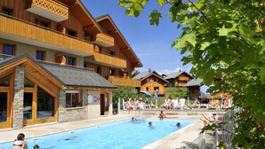 Et poolområde med flere swimmingpools, hytter i træ og folk, der slapper af ved poolen.