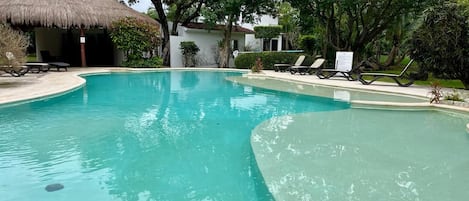 A swimming pool with lounge chairs and a thatched-roof structure.