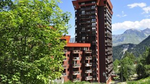 A multi-story building with balconies, surrounded by lush greenery and mountains in the background. - 200m from ski slopes, fitness, swimming pool, sauna, terrace, balcony, tv, ski locker, 35-40m² (Le Corbier)