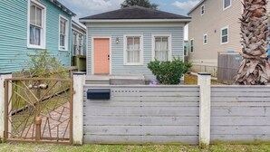 Il s’agit d’une propriété résidentielle dotée d’une entrée sécurisée par un portail, d’une petite maison à la façade bleu clair, d’une porte de couleur pêche et d’une clôture en bois.