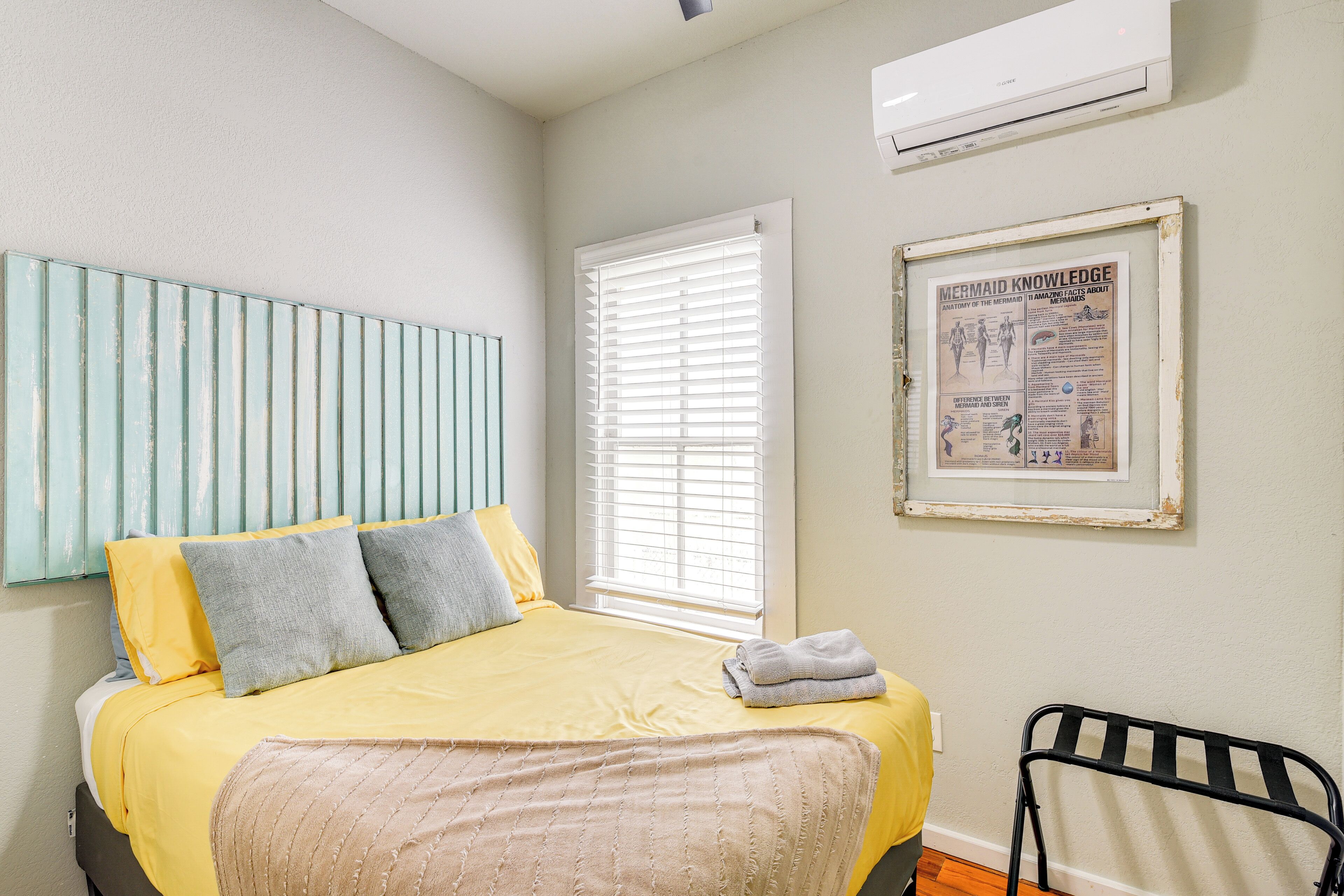 A bedroom with a bed, a window with blinds, a radiator, and a framed poster on the wall.