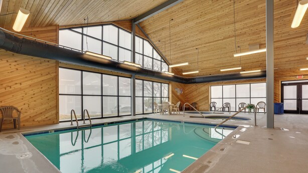Une piscine intérieure avec des parois en verre transparent, un plafond en bois et un sol en béton.