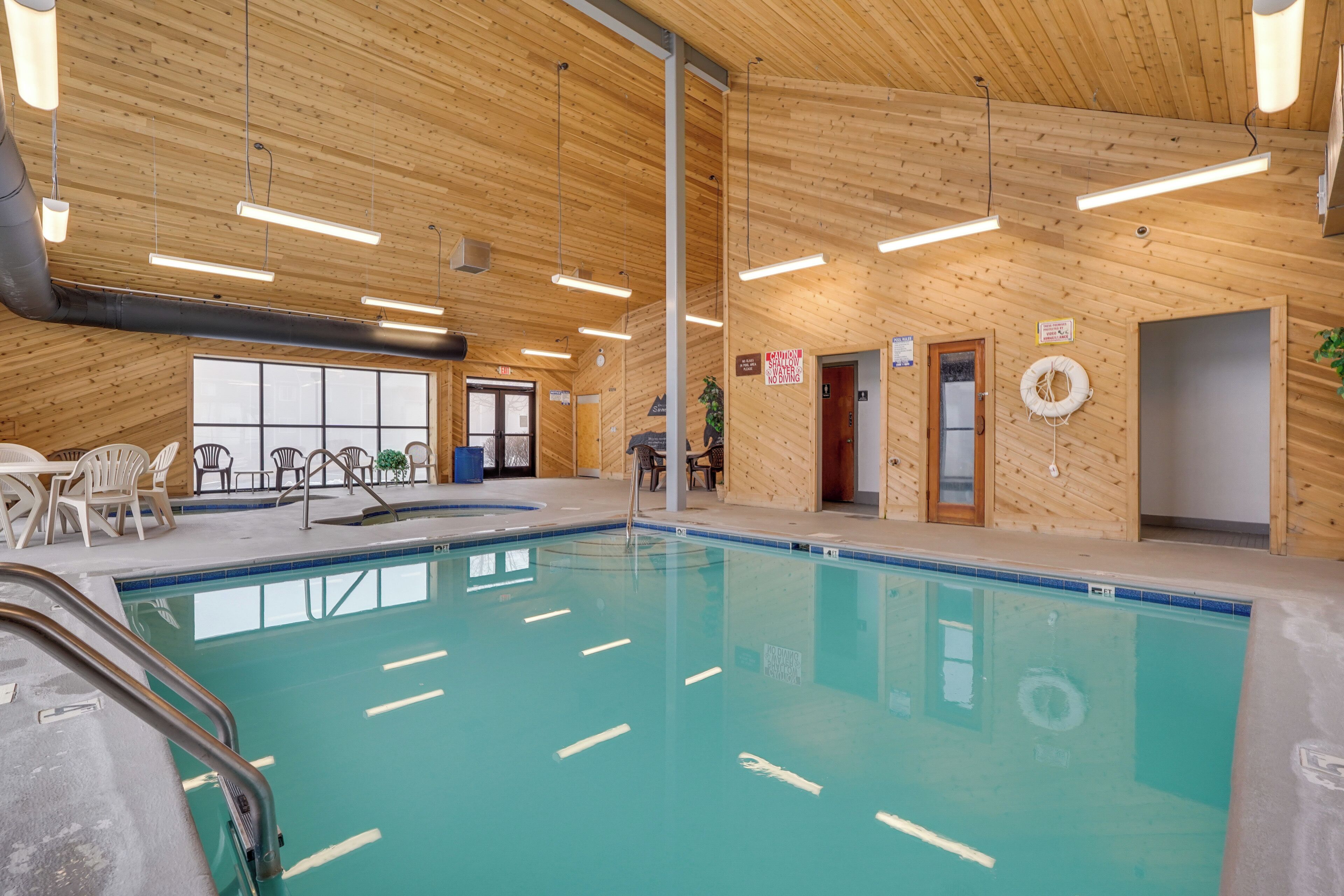 An indoor swimming pool with wooden walls and ceiling, clear signage, and basic amenities.