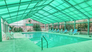 Ein überdachter Pool mit Liegestühlen und einem Tisch, umgeben von Glaswänden.