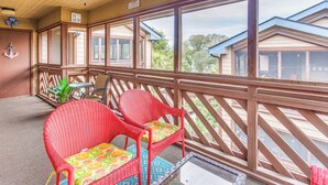 Eine überdachte Veranda mit Korbstühlen und einem Tisch, Holzgeländern und Blick auf Häuser im Hintergrund.