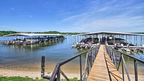 Un muelle de madera que conduce a un puerto deportivo con barcos amarrados bajo estructuras cubiertas.