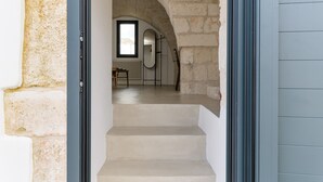 A stone archway leading to a room with a window, a radiator, and a chair.