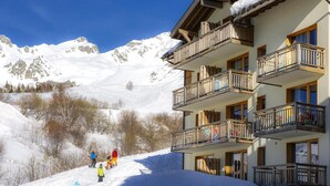 Um edifício com várias andares e varandas, cercado por montanhas cobertas de neve.