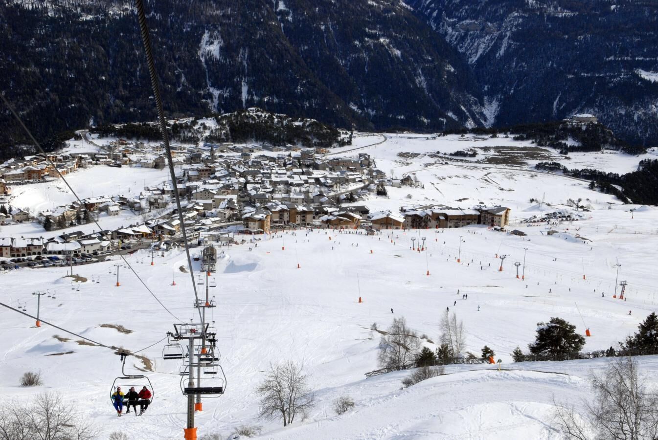 Une station de ski enneigée, avec un télésiège, des bâtiments et un paysage montagneux en arrière-plan.