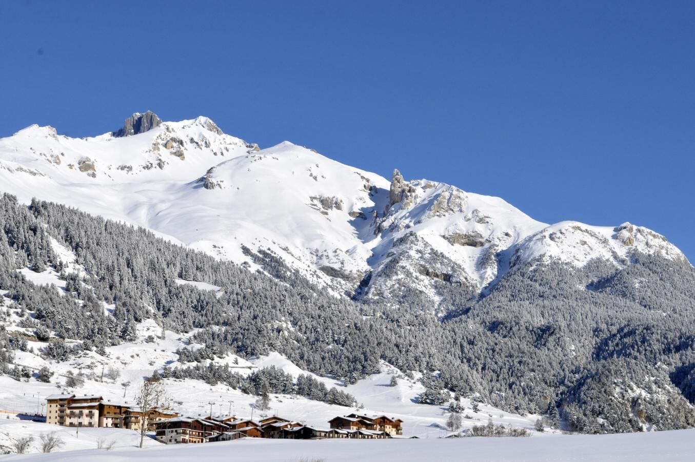 Ein mit Schnee bedeckter Berg mit einem Skiort im Vordergrund, mit Gebäuden im Chalet-Stil.