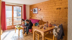 Une pièce chaleureuse aux murs en bois, avec une table à manger et des chaises, un lit et un balcon agrémenté de rideaux rouges.