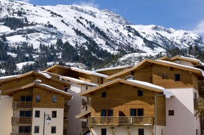 Un conjunto de chalés de madera en la montaña, con balcones, frente a laderas nevadas y pinos.