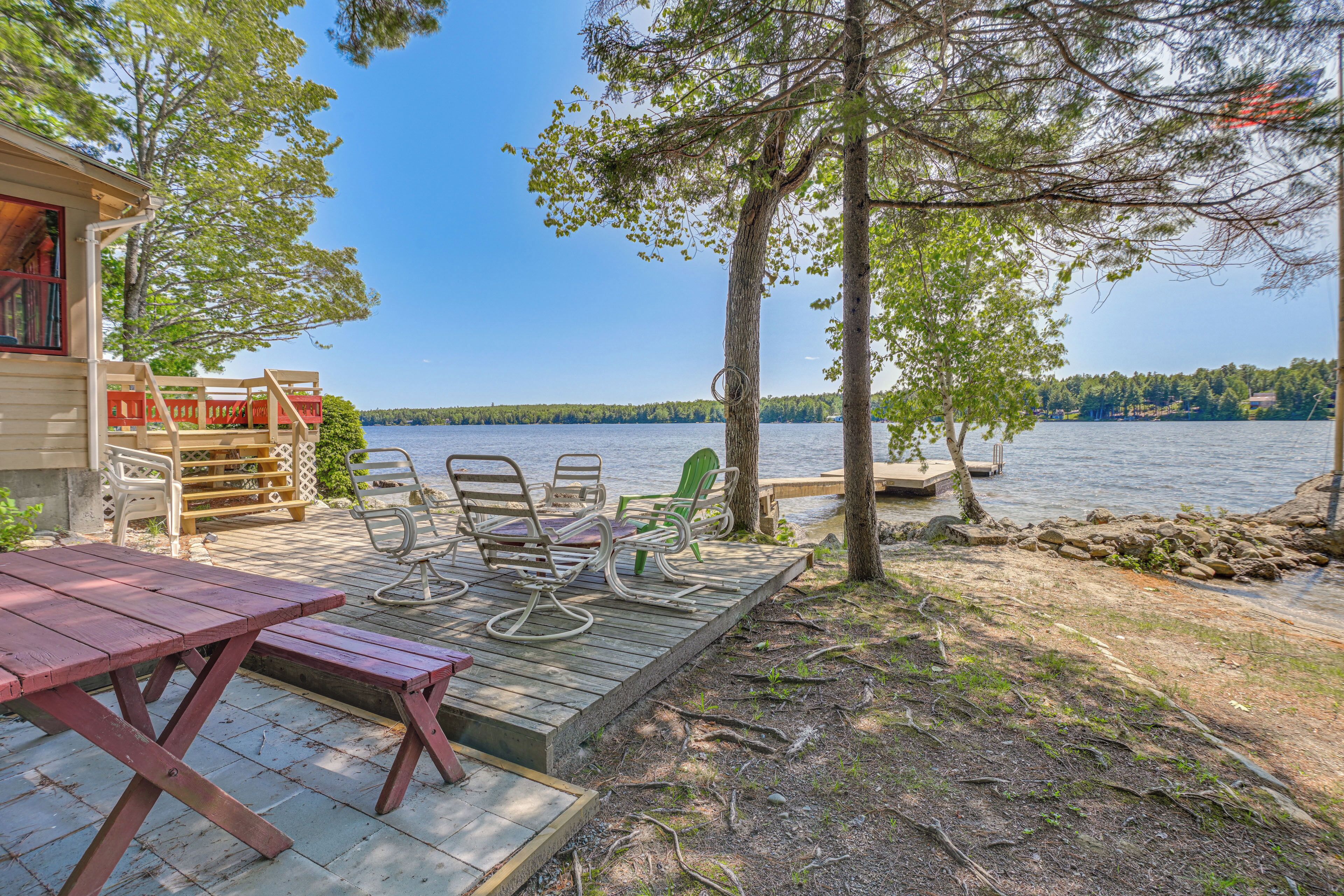 A wooden deck with outdoor furniture, a view of a lake, and a dock extending into the water.