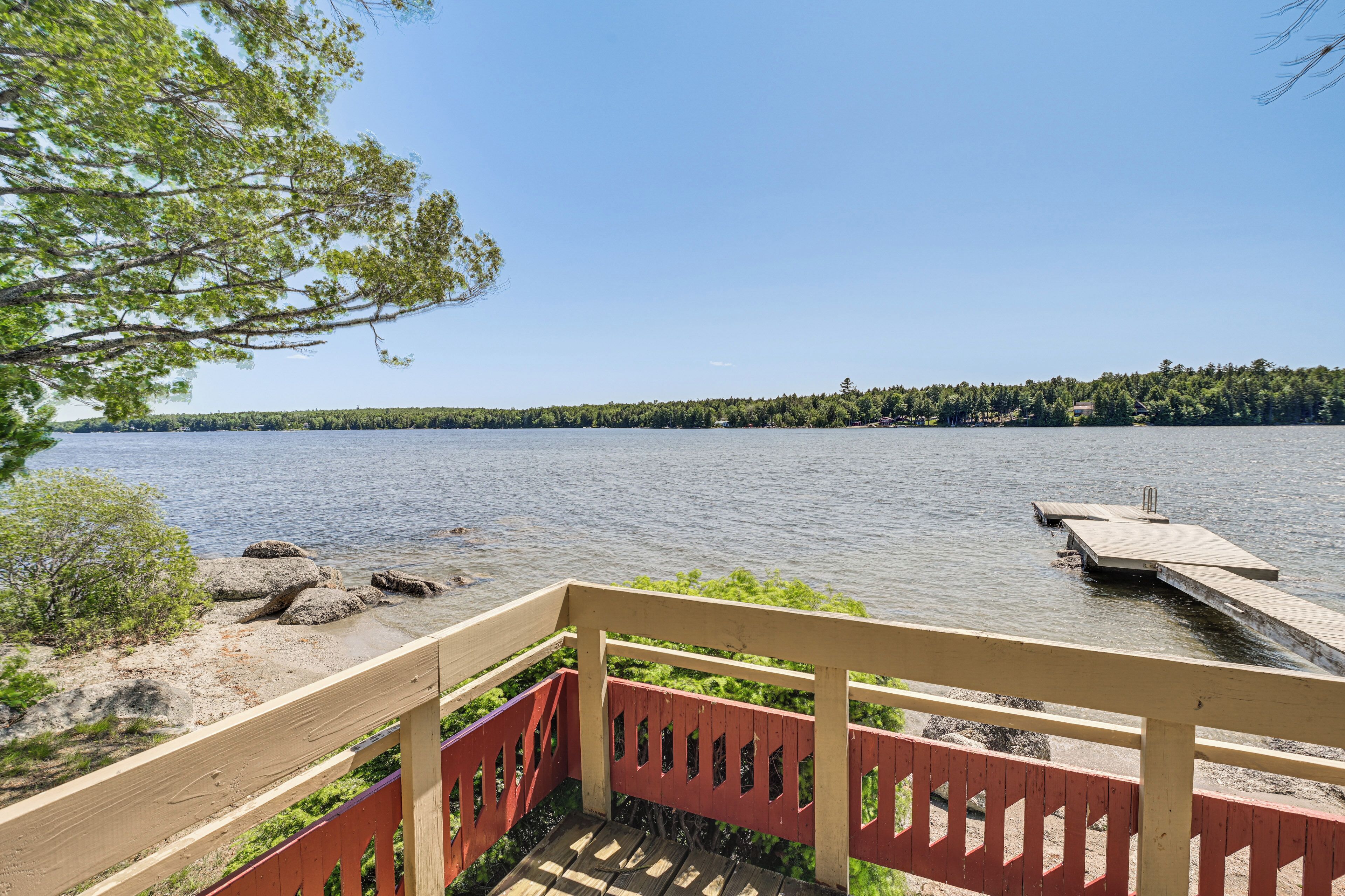 Une terrasse en bois offrant une vue sur un lac paisible et une jetée s’avançant dans l’eau.
