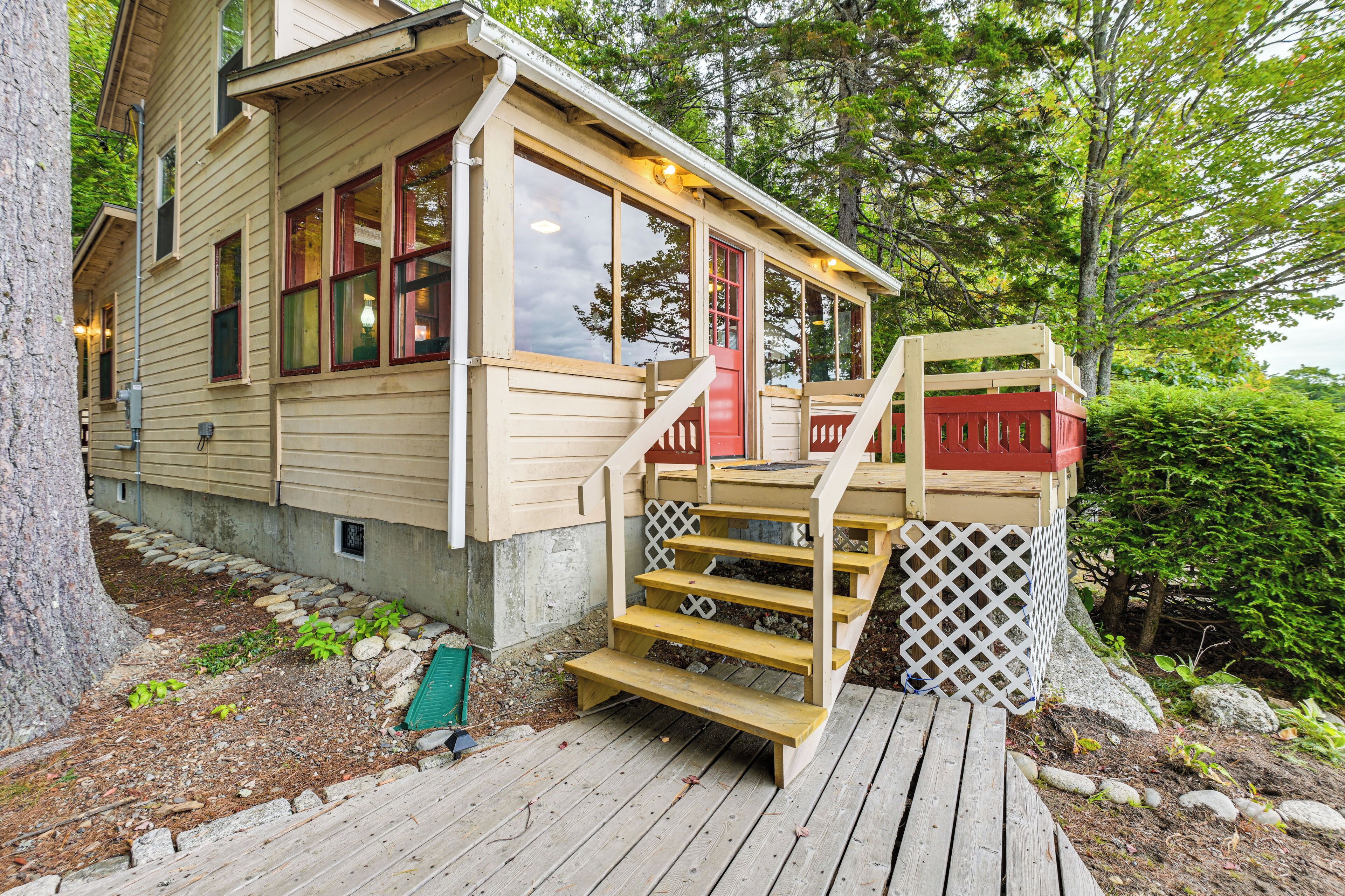 A wooden cabin with a porch and steps leading to a red door.