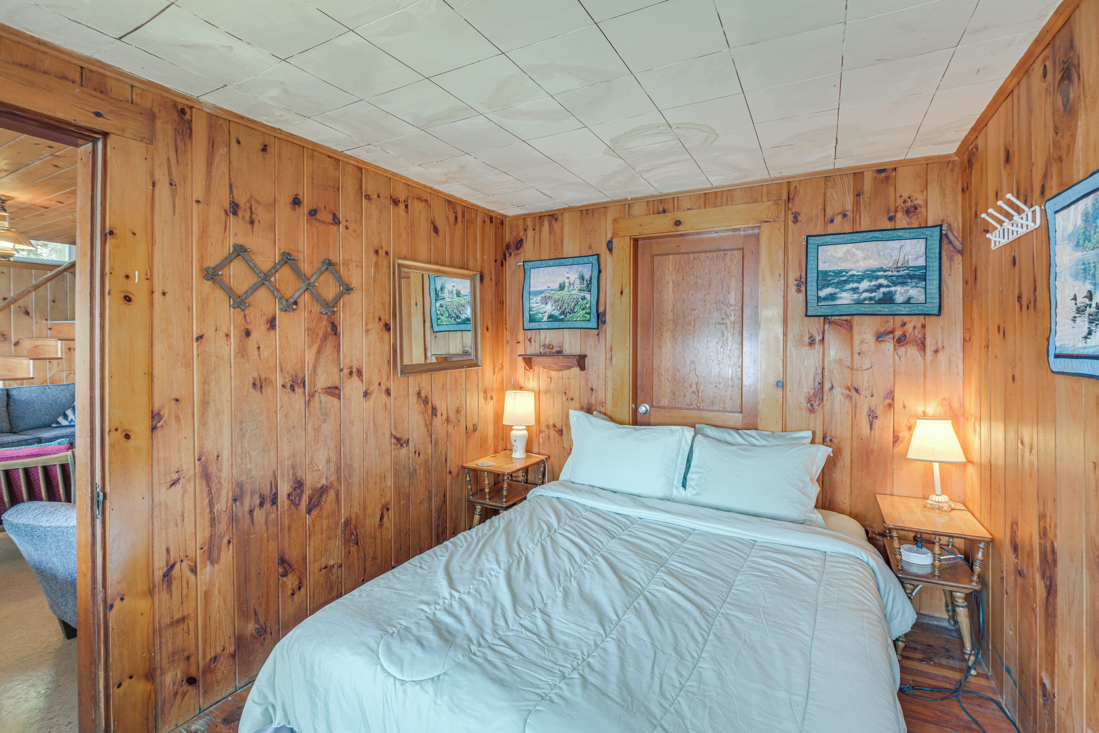 A wooden-paneled room with a bed, two nightstands with lamps, and framed pictures on the walls.