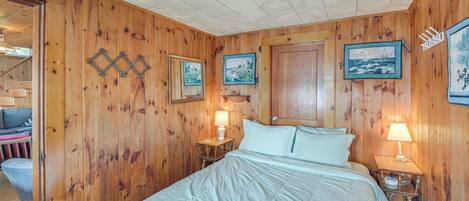 A wooden-paneled room with a bed, two nightstands with lamps, and framed pictures on the walls.