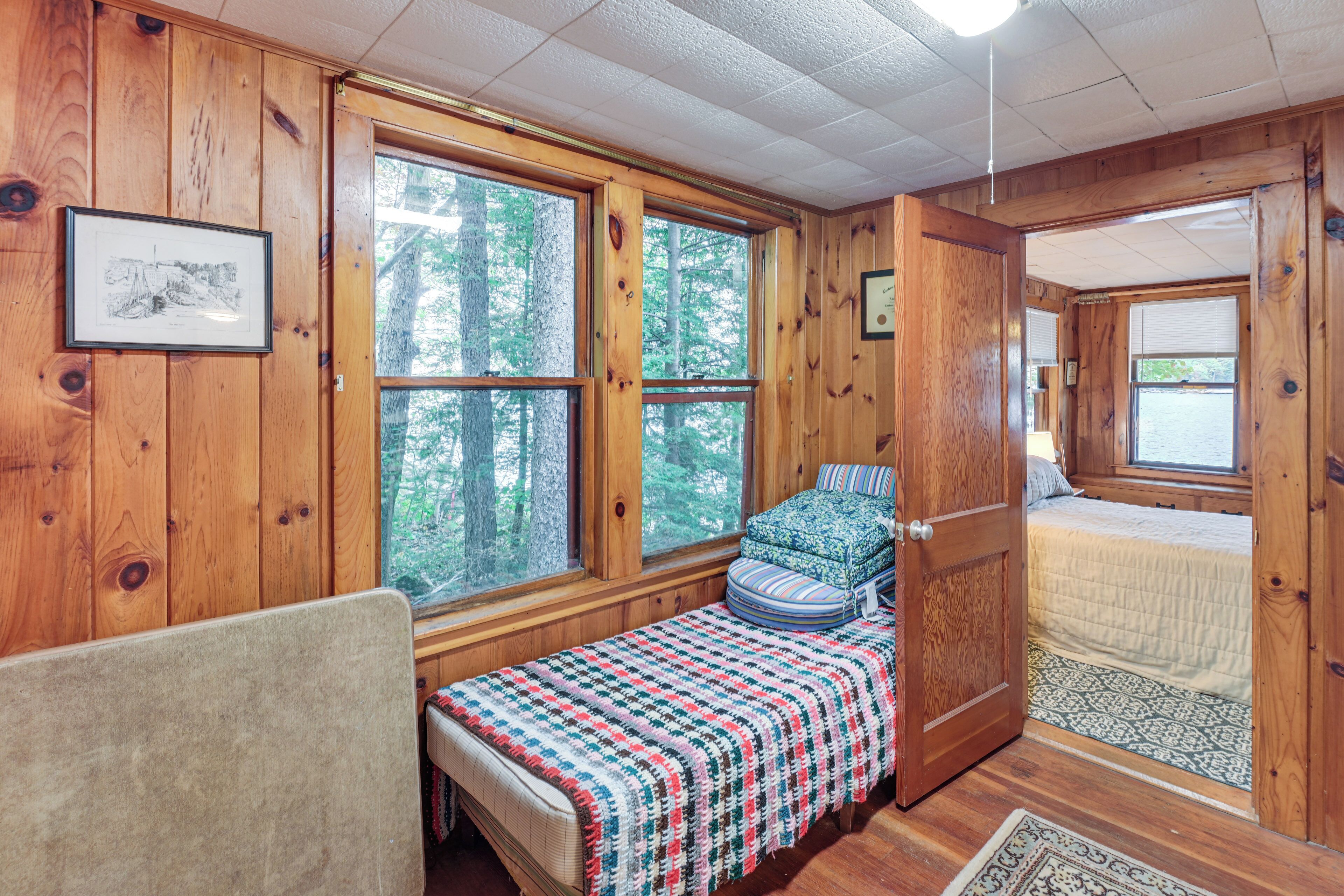 A cozy cabin room with a bed, a bench with a blanket, and large windows offering a view of the forest.