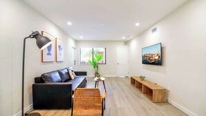 A modern living room with a black leather sofa, a floor lamp, a TV, and a large window with a cityscape view. - Prime Miami Location | Free Parking (Miami)