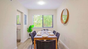 A dining area with a table set for six, surrounded by wicker chairs, a potted plant, and a large window with blinds. - Prime Miami Location | Free Parking (Miami)