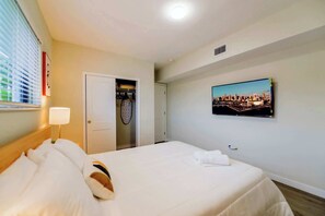 Ein Hotelzimmer mit einem Bett, einer Nachttischlampe, einer Tür zu einem Schrank und einem Stadtbild an der Wand.