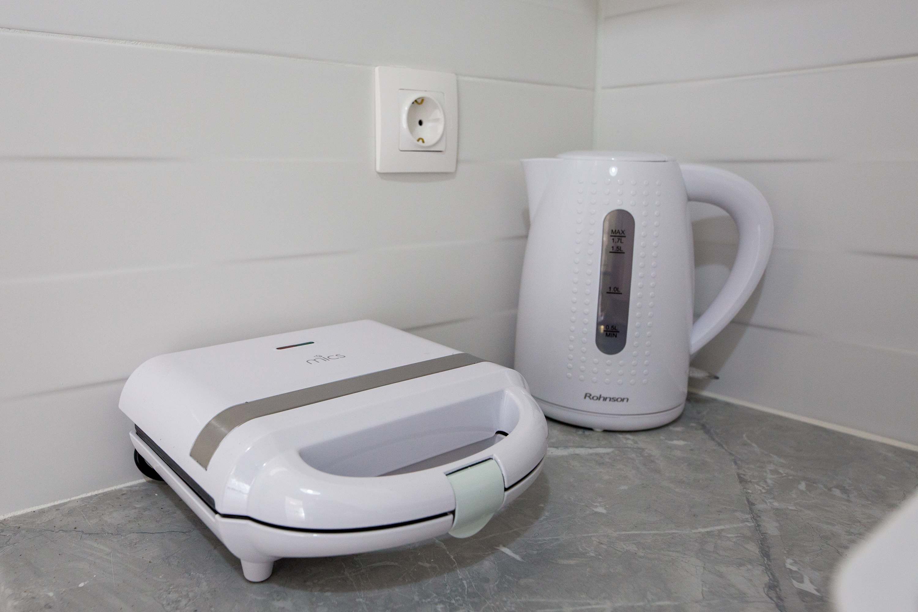 A white electric kettle and a white electric toaster on a marble countertop.