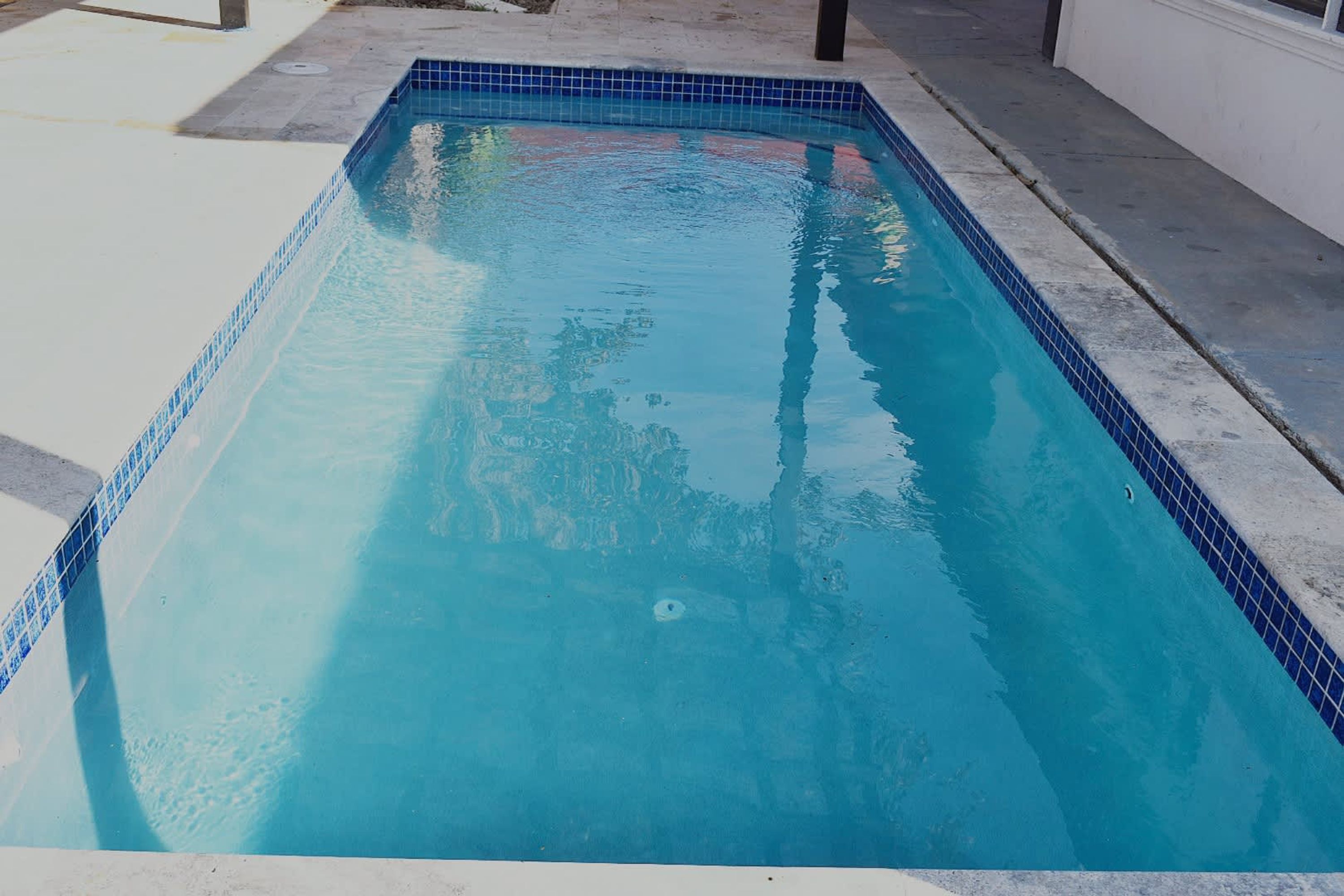 A rectangular swimming pool with blue tiles on the edges, surrounded by a concrete deck.