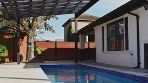 Una piscina con borde de azulejos, una pérgola y un muro de ladrillo al fondo.