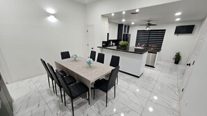 Una cocina moderna con una isla central, paredes blancas y una zona de comedor con piso de baldosas de mármol.