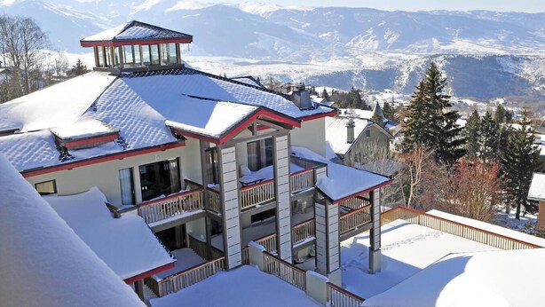 Ein mehrstöckiges Gebäude mit Balkon, umgeben von schneebedeckten Bergen.