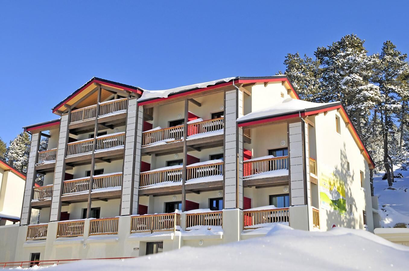 Et hotel med flere etager, altaner, et rødt tag og sne på jorden.