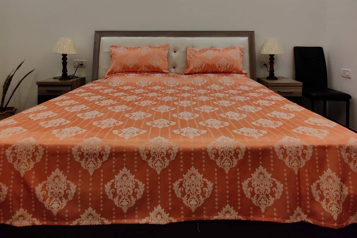 A bedroom with a large bed, two bedside tables with lamps, a ceiling fan, and a potted plant.