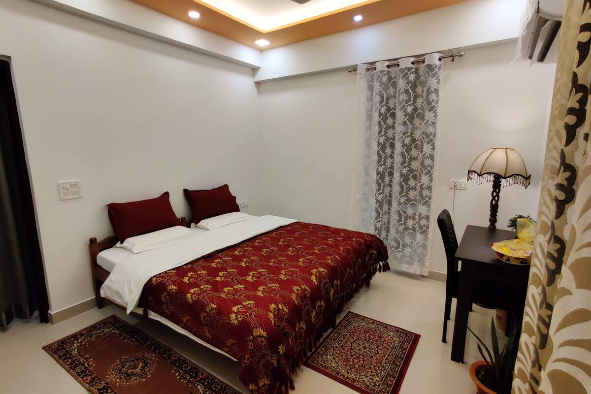 A bedroom with a bed, a desk, a chair, a lamp, and a potted plant.
