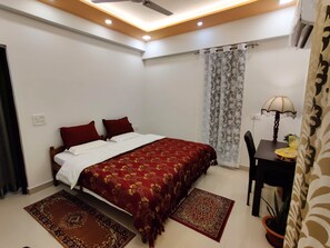 A bedroom with a bed, a desk, a chair, a lamp, and a potted plant. - Anand's Aashiyana Homestay (Agra)