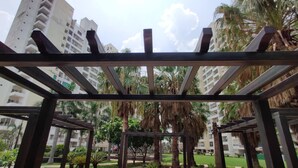 A covered outdoor area with a pergola structure, surrounded by palm trees and a well-maintained lawn. - Anand's Aashiyana Homestay (Agra)