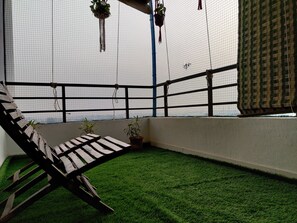 A balcony with artificial grass, a wooden bench, potted plants, and a view through a netted window. - Anand's Aashiyana Homestay (Agra)