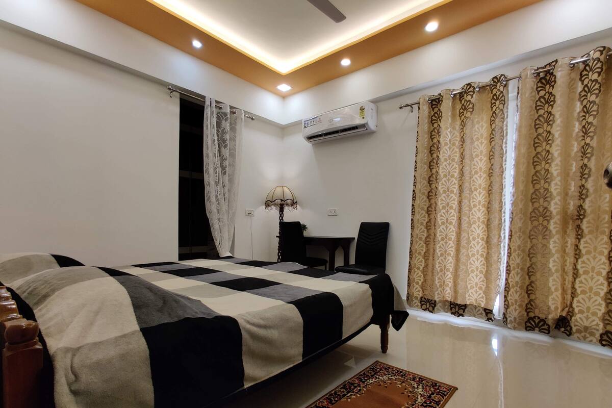 A bedroom with a bed, a desk, a chair, an air conditioner, and curtains.