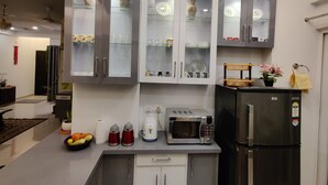 A modern kitchen with built-in cabinets, a microwave, a refrigerator, and a countertop with a fruit bowl and kettles. - Anand's Aashiyana Homestay (Agra)