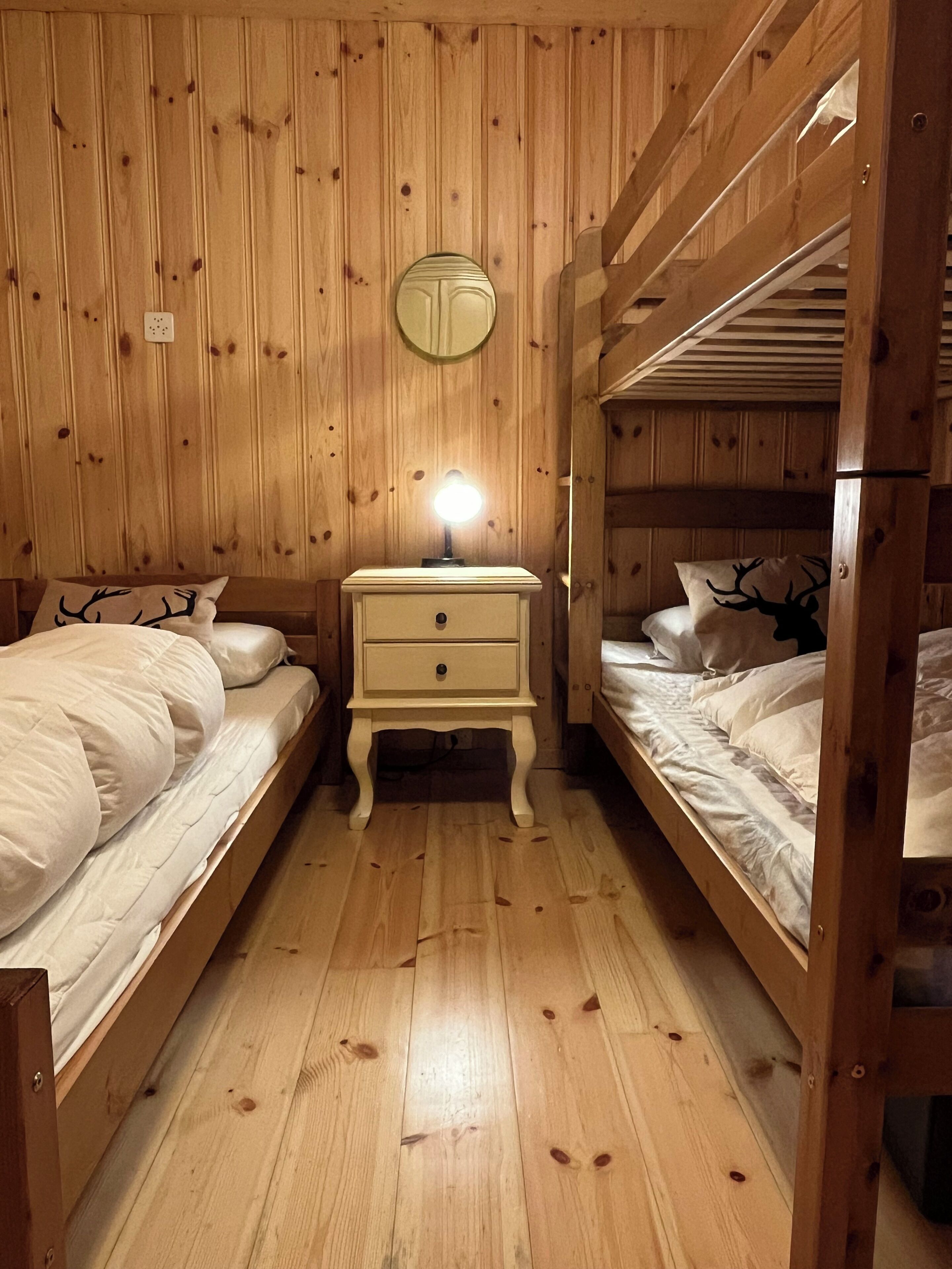 A wooden room with bunk beds, a bedside table with a lamp, and a mirror on the wall.