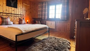 A wooden room with a bed, a fur rug, a wooden dresser, and a window with curtains. - Chalet Gallois, your perfect winter escape very close to the slopes! (Nendaz)