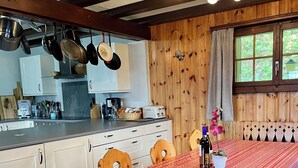 A cozy kitchen with wooden walls, white cabinets, and a dining area with a red patterned tablecloth. - Chalet Gallois, your perfect winter escape very close to the slopes! (Nendaz)