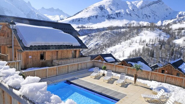 Un chalet de madera con piscina y sillas de descanso, rodeado de montañas nevadas.