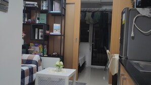 A compact living space with a kitchenette, a dining area with a table and chairs, a bookshelf, and a small trash bin. - 5-Minutes Walk to Mall of Asia, One-bedroom with Balcony at Shell Residences (Pasay)