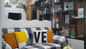 A cozy living room with a plaid sofa, a white coffee table, and a bookshelf filled with books and decorative items. - 5-Minutes Walk to Mall of Asia, One-bedroom with Balcony at Shell Residences (Pasay)