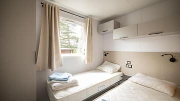 A single bed with a headboard, a window with curtains, and a wall-mounted shelf above the bed.