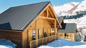 Eine Holzhütte mit Balkon vor einer verschneiten Berglandschaft.
