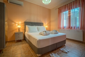 A bedroom with a bed, bedside lamps, a radiator, and a window with curtains. - Villa Clairy 3-bedroom Villa With Private Pool (Zakynthos)