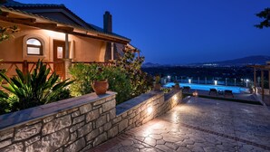 Une maison avec un mur en pierre, une piscine et une vue sur la ville la nuit.